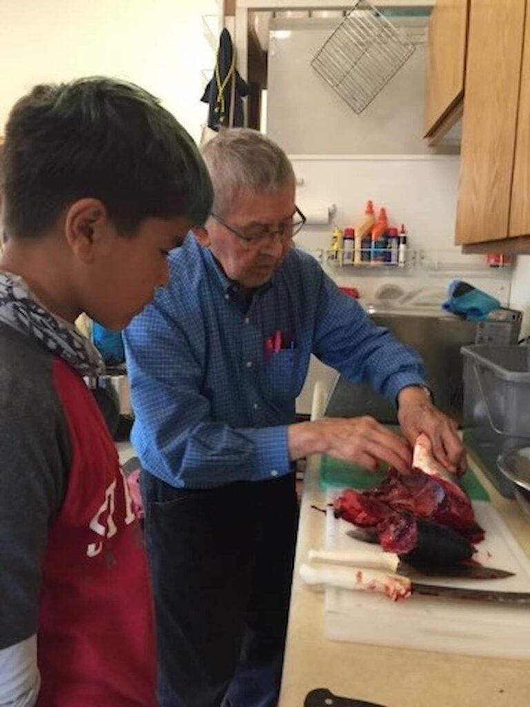 Fish cutting: K’alaagáa Íihlangaa (Nathaniel) Blake, learning from his great great uncle, Dennis Demmert, how to clean, filet, and prepare a salmon.